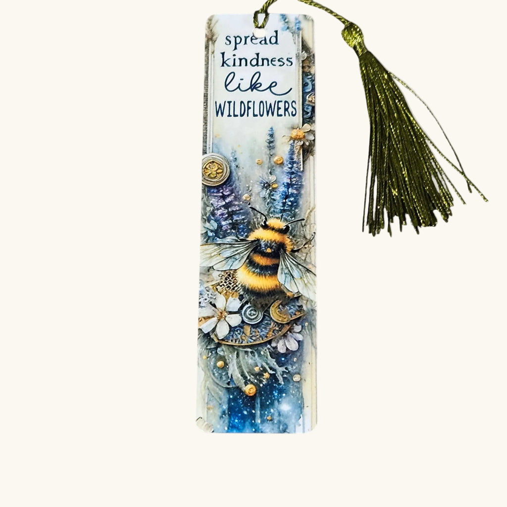 A decorative paper bookmark with a tassel, featuring a whimsical illustration of a bumblebee, wildflowers, and blue-toned floral artwork. The top reads, 'spread kindness like WILDFLOWERS.