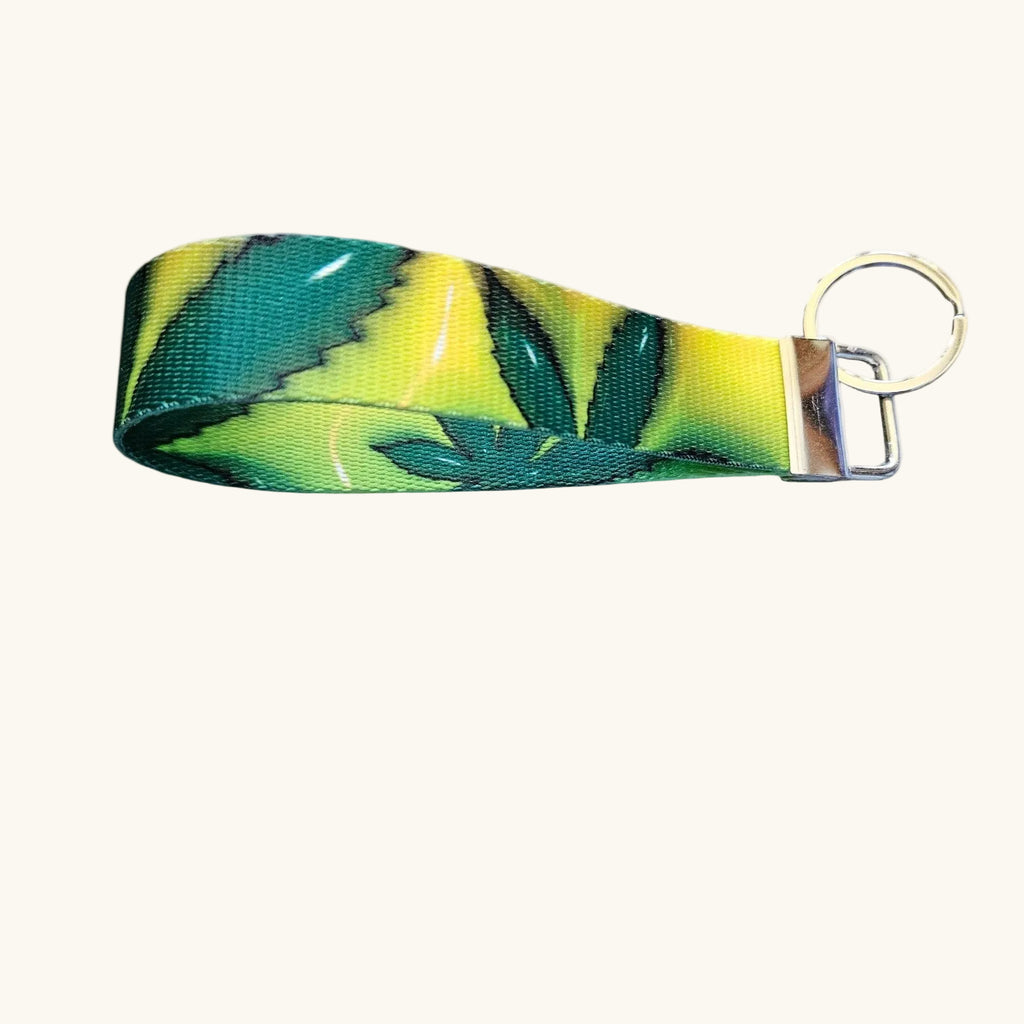 A fabric keychain strap featuring a green and yellow leaf pattern, attached to a silver metal split ring, shown against a plain off-white background.