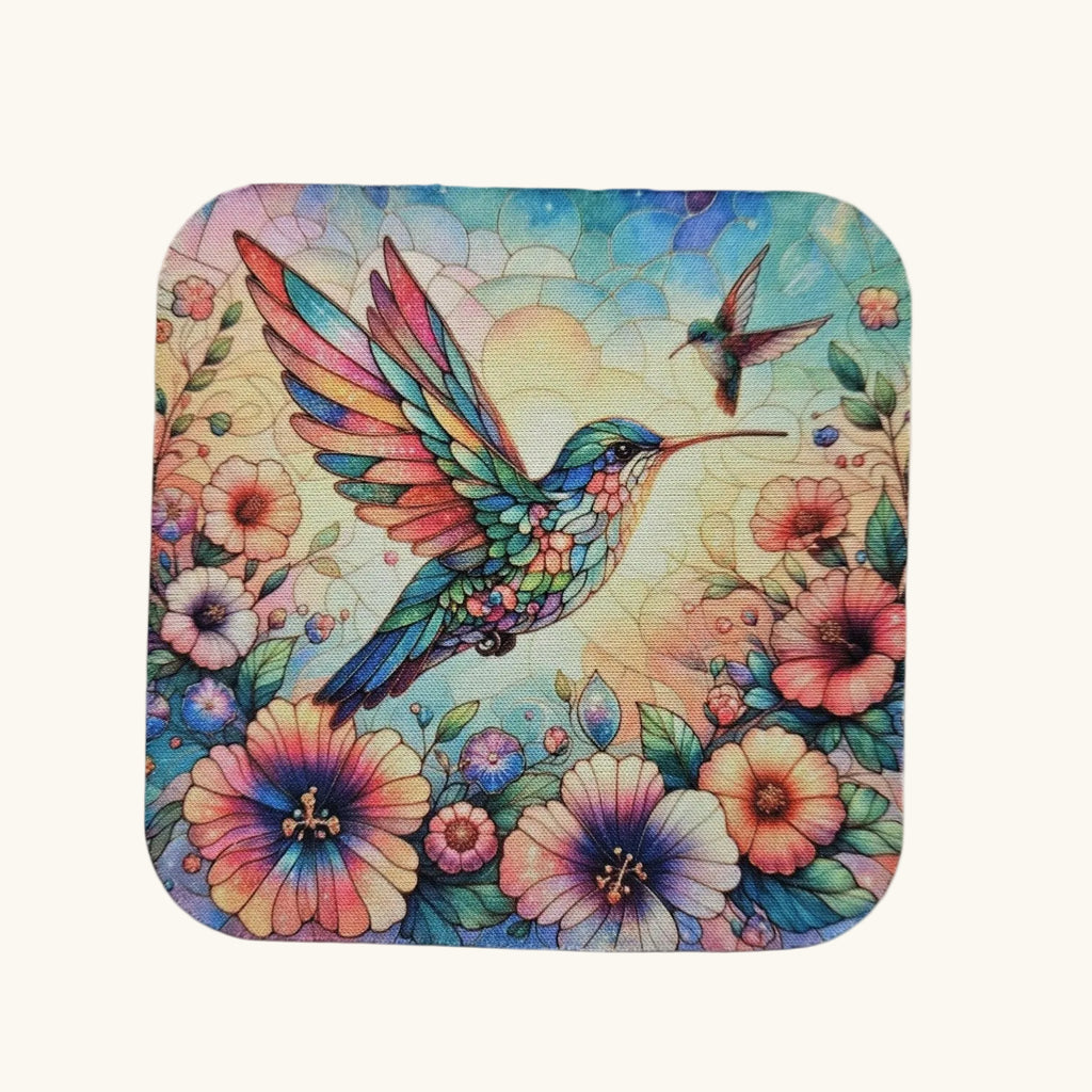 A square coaster with rounded corners featuring a colorful, detailed illustration of a hummingbird and flowers on a light cream background.