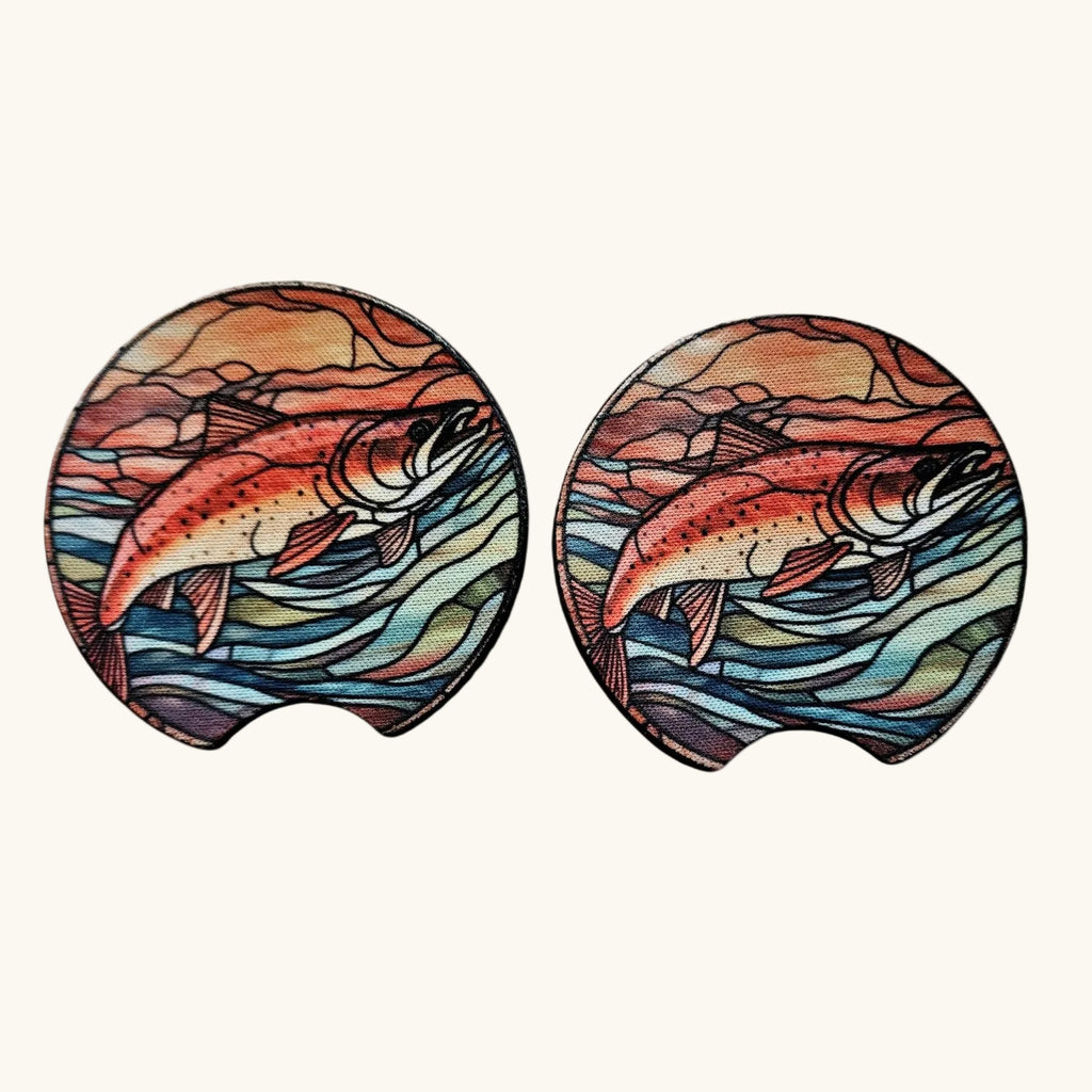 Two oval coasters with a stained-glass style illustration of a salmon fish over blue and green water waves, set against a light beige background.